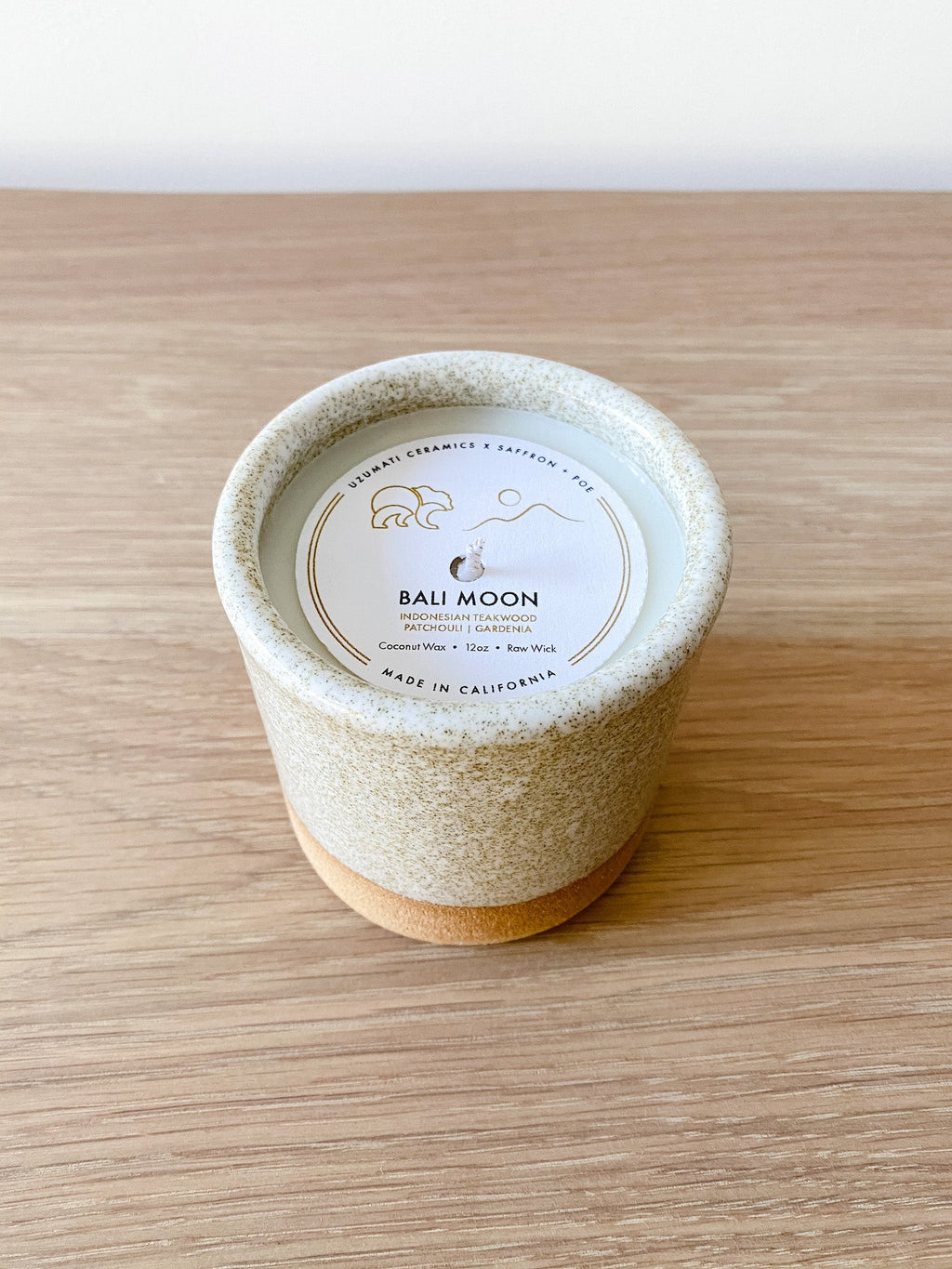 Uzumati Ceramic Bali Moon Candle in rustic stoneware vessel with speckled white glaze on wooden surface