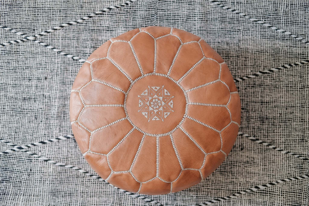Embroidered Moroccan leather pouf with geometric stitching on patterned rug