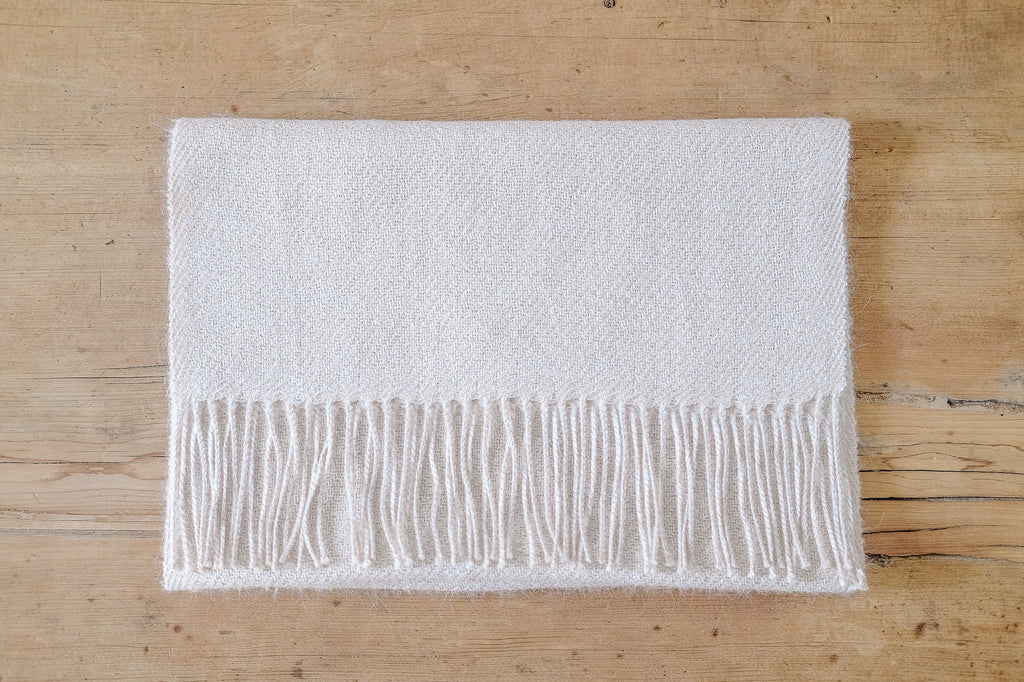 Beige baby alpaca scarf with long twisted fringe on wooden surface