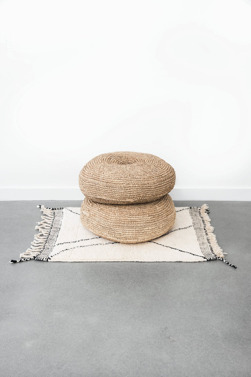 Natural woven hyacinth pouf stacked on patterned rug with concrete floor background