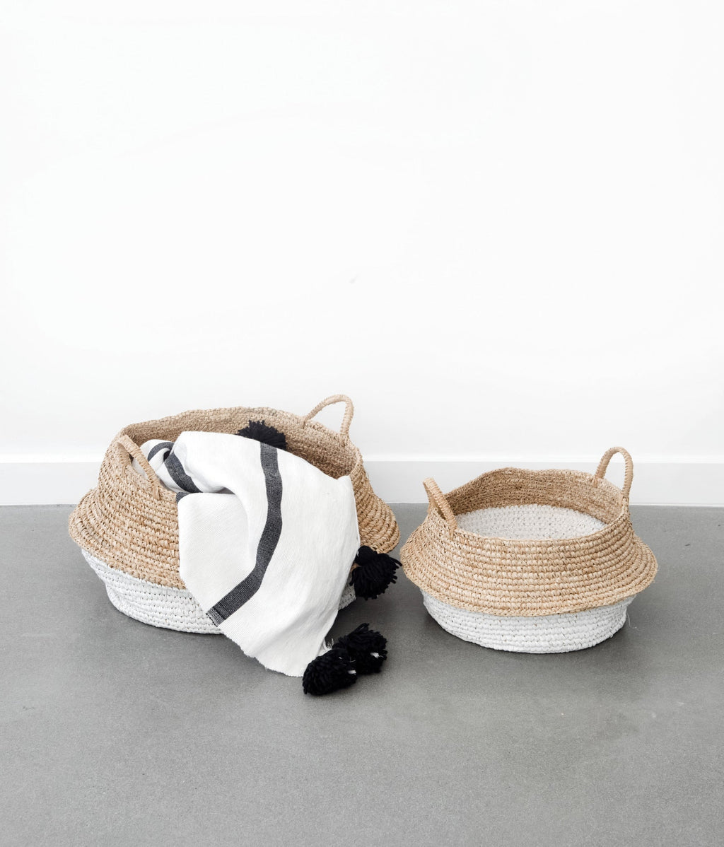 Two-toned collapsible woven hyacinth baskets with a white and natural finish, one holding a black and white striped cloth.