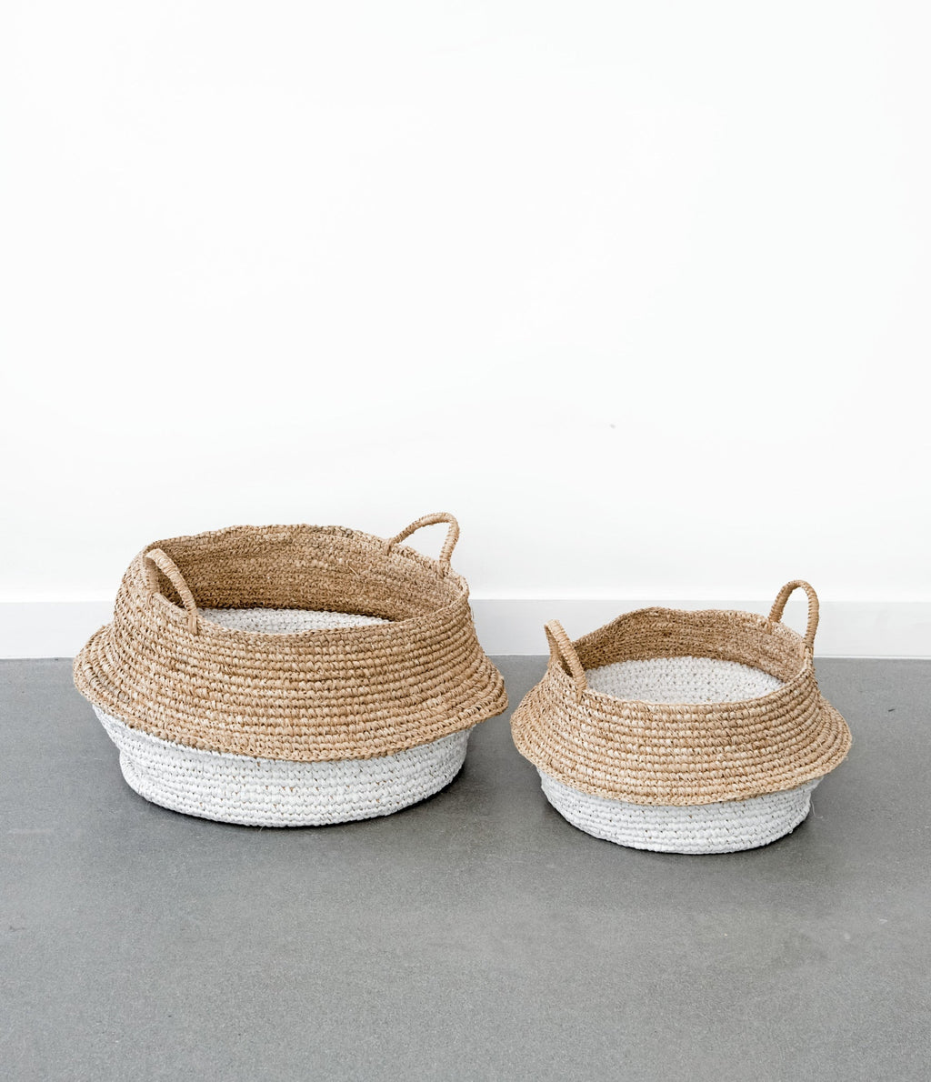 Two-toned collapsible woven hyacinth baskets with handles on a gray floor against a white wall