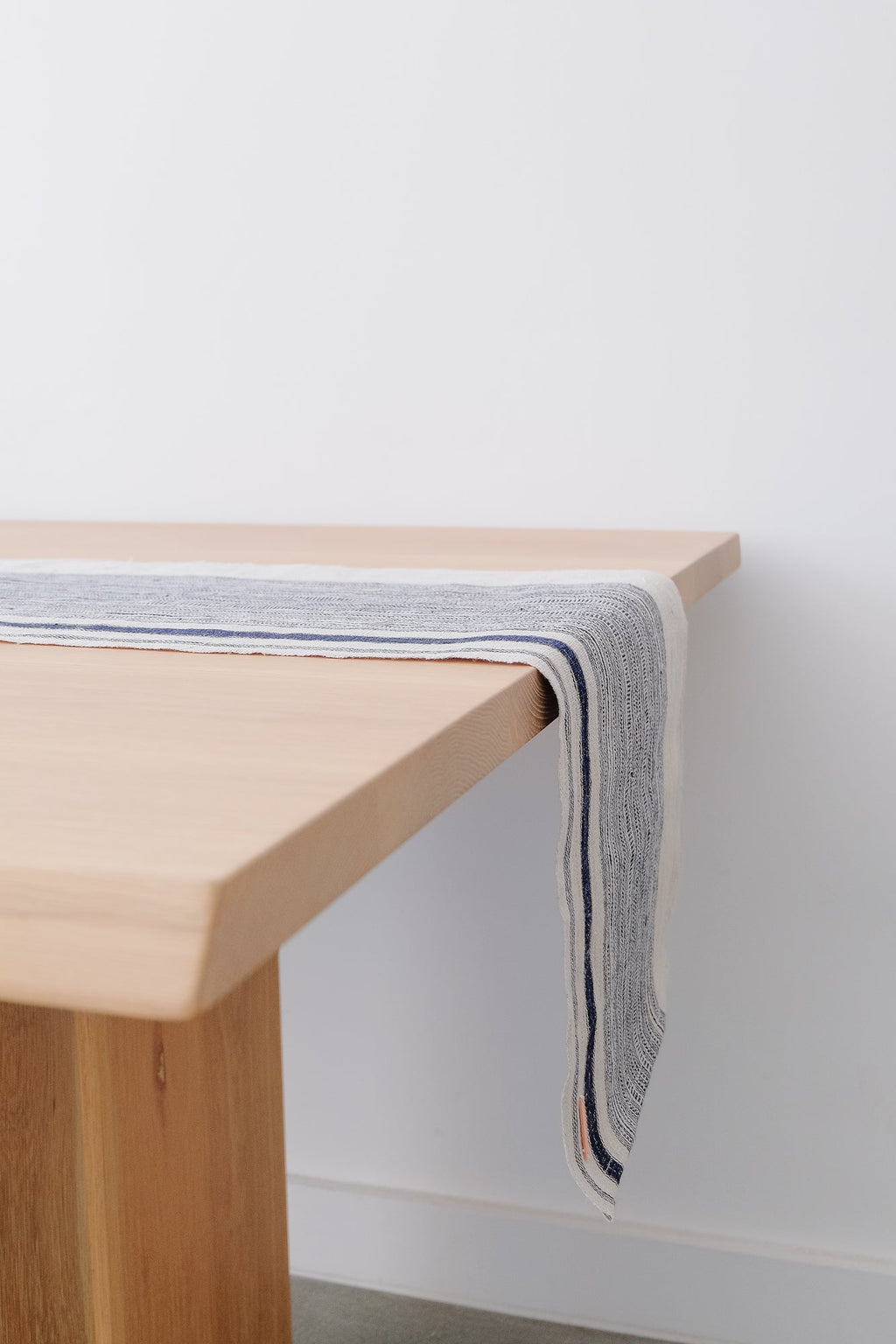 Vintage striped table runner in indigo and cream draped over light wooden table edge