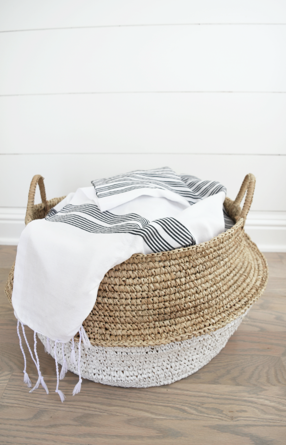 Collapsible woven hyacinth basket with white and black striped fabric inside on wooden floor