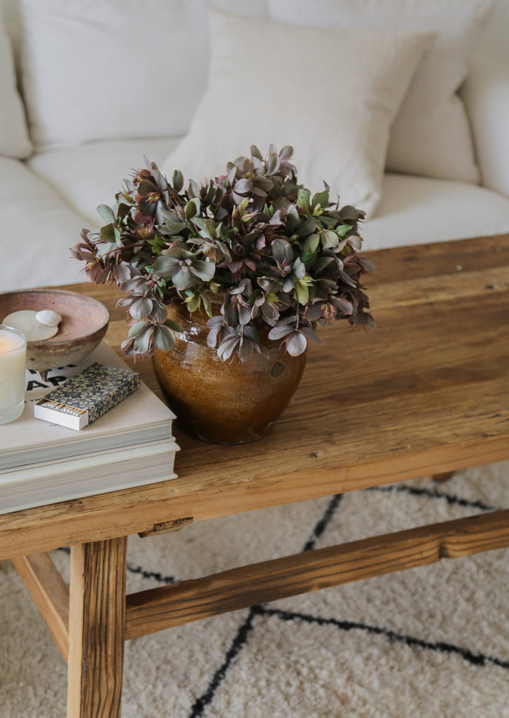 Zoomed in view of Vintage Wood Coffee Table in a living room setting with floral plant on a Beni Ourain Rug. - Saffron + Poe