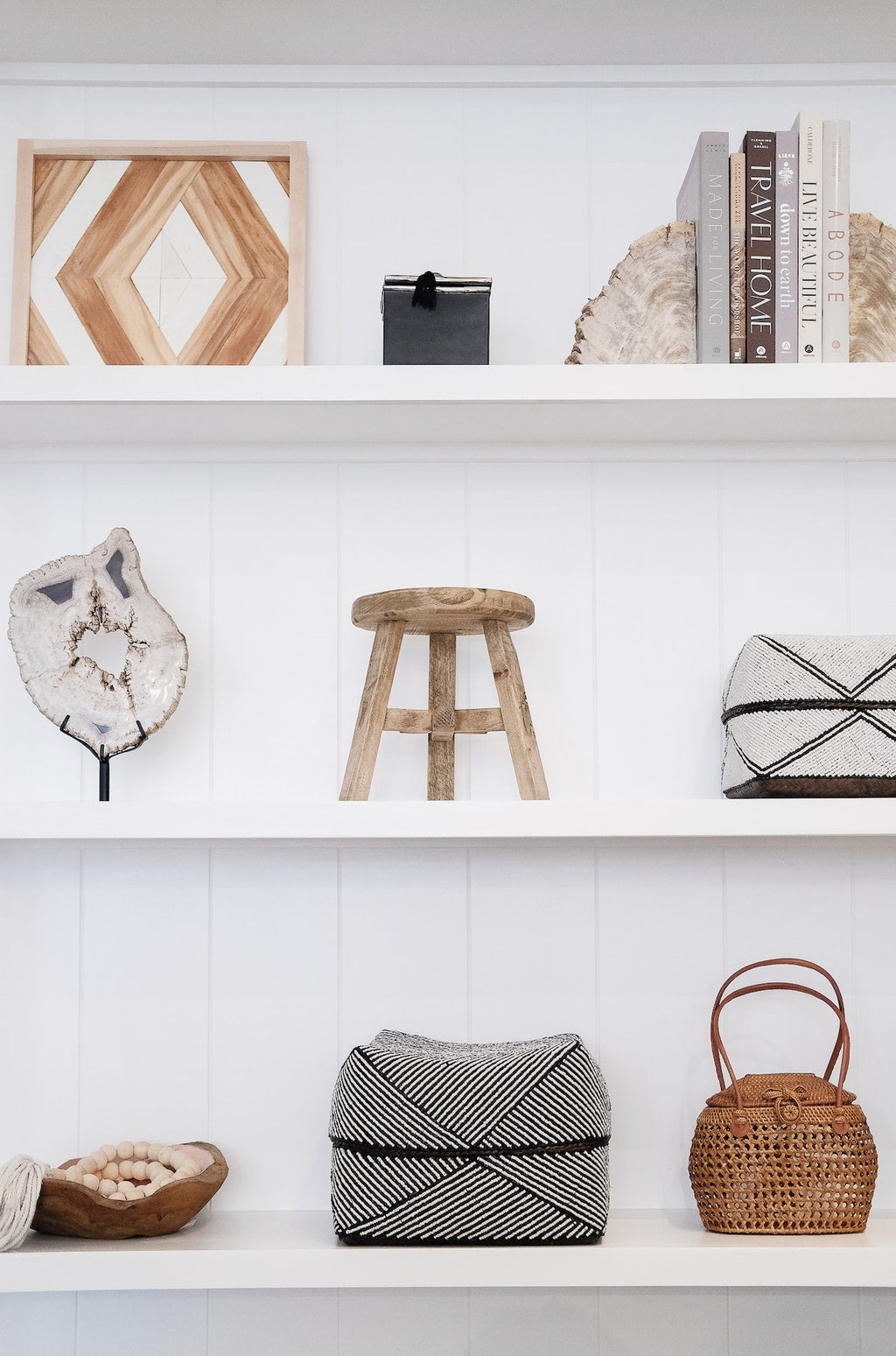 Petite vintage wooden stool displayed on white shelf with decorative items in minimalist setting