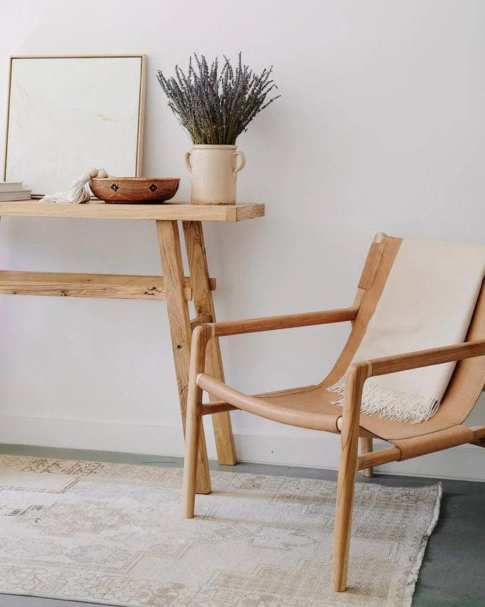 Handcrafted vintage console made from reclaimed elmwood styled with vase and books next to a wooden chair in minimalist room