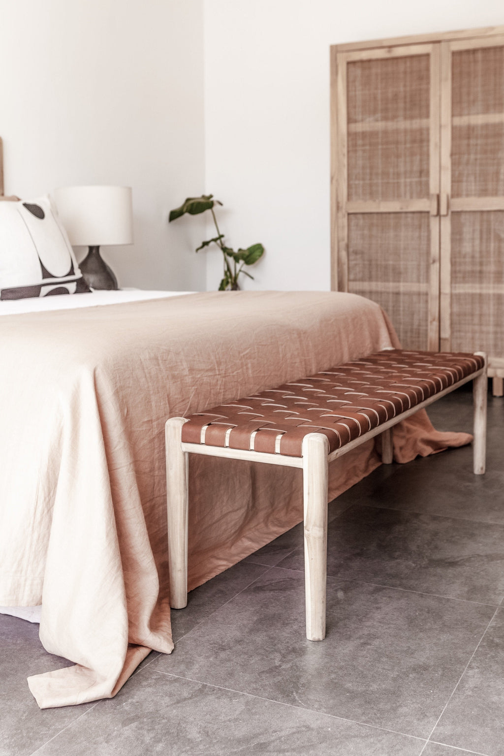 Woven leather bench with teak frame and saddle leather straps in a modern bedroom setting